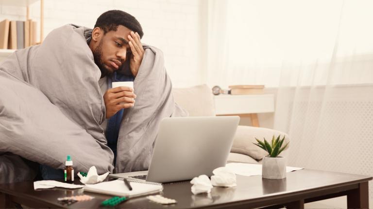 man wrapped in blanket looking at laptop